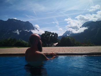 Man sitting by swimming pool against sky