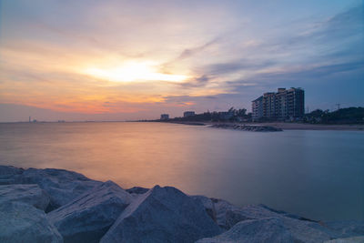 Scenic view of sea by buildings against sky during sunset