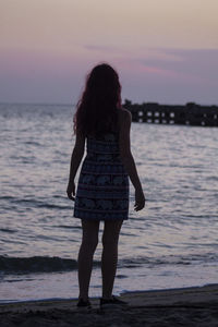Rear view of woman standing on beach during sunset