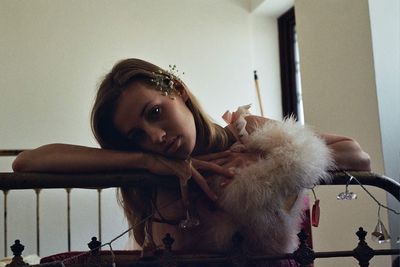 Portrait of woman with fake fur leaning on railing against wall at home