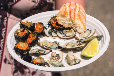 Tourist showing a plate with raw sea urchins and oysters ready to eat with bread and lemon in bari