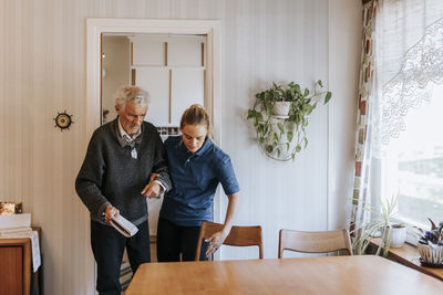 Female caregiver assisting senior man while walking at home