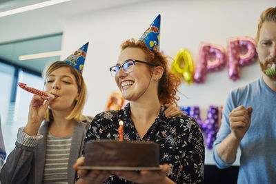 Colleagues having a birthday celebration in office with cake, party blower and party hats