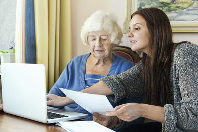 Grandmother and granddaughter with document using laptop at home