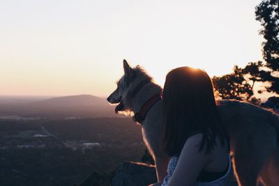 Side view of woman sitting with dog on mountain against clear sky during sunset