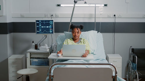 Portrait of young woman using mobile phone while sitting at clinic