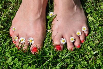 Low section of woman standing on grass with flowers