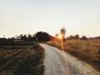 Empty road amidst field against clear sky during sunset