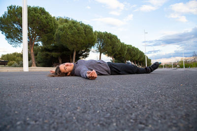 Portrait of man lying on road against trees and sky