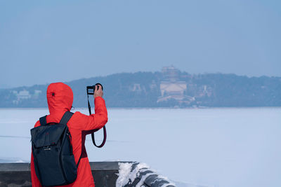 Rear view of person standing by sea against sky during winter