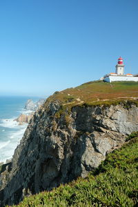 Lighthouse by sea against clear blue sky