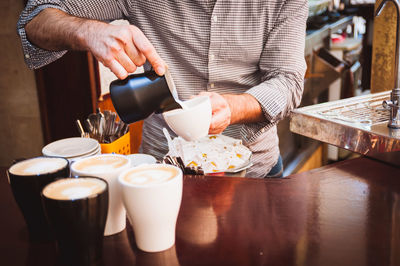 Midsection of barista pouring cream in coffee cup at cafe