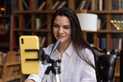 Happy young caucasian millennial or gen z woman with long brunette hair streaming with smart phone 