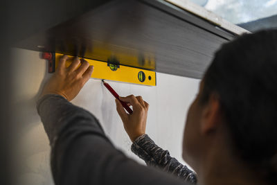 Female carpenter using bubble level and marking on wall with pencil