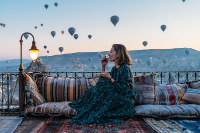 Woman drinking early morning tea with hot air balloons in cappadocia