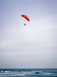 Distant view of person paragliding over sea against sky