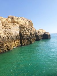 Rock formations by sea against clear blue sky