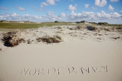 Close-up of text on sand at beach against sky