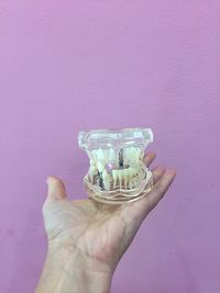 Close-up of hand holding dentures against colored background