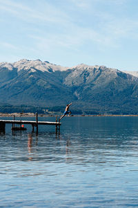 Jumping from a pier with a scenic view of sea and mountains against sky