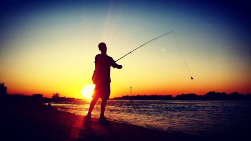 Silhouette man fishing at beach against sky during sunset