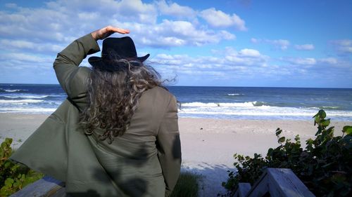 Rear view of man wearing hat at beach against sky