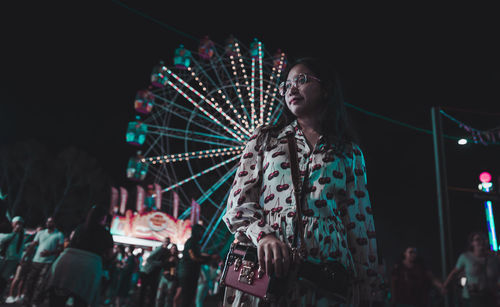 Low angle view of woman standing against ferris wheel at night