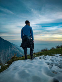 Rear view of man standing on mountain against sky