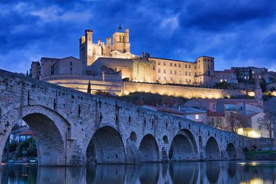 Arch bridge in city against sky at dusk