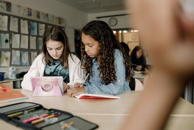 Female students using tablet at table in classroom