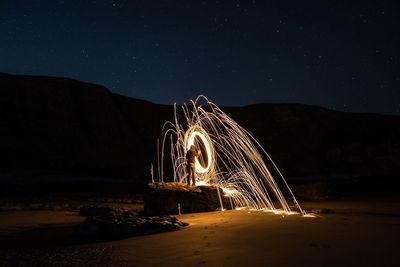 Illuminated ferris wheel on land against sky at night