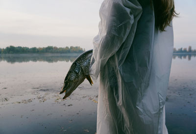 Woman holding fish while standing at lake