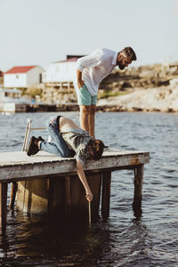 Son fishing with stick in sea while father standing on pier against sky