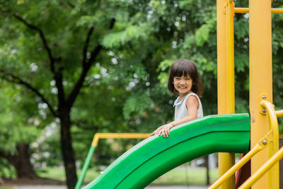 Full length of smiling girl looking away while moving on slide in playground