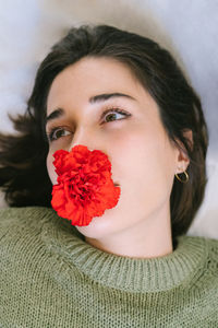 From above of tranquil female with dark hair and blooming red carnation in mouth