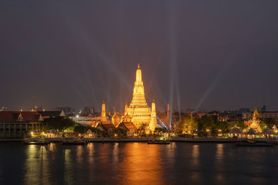 Illuminated buildings by river against sky at night