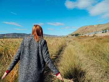 Rear view of woman walking on field against sky