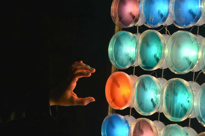 Cropped hand of woman reaching towards illuminated lighting equipment against black background