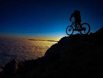 Low angle view of silhouette man riding bicycle on rock