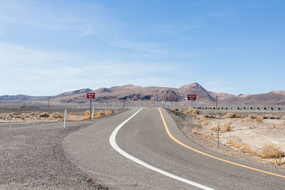 Empty road leading towards mountains against sky on sunny day