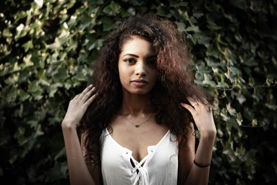 Portrait of beautiful young woman standing against plants