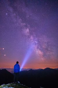 Rear view of man standing with flashlight against star field at night