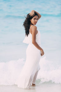 Portrait of young woman standing at beach against sky