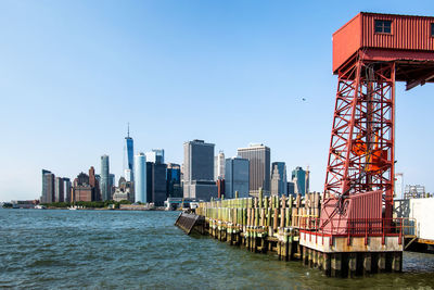 Tower by sea against buildings in city against clear sky