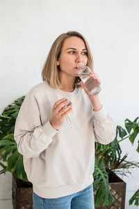 Young blonde woman is holding a glass bottle of water and drinking, healthy lifestyle,water balance