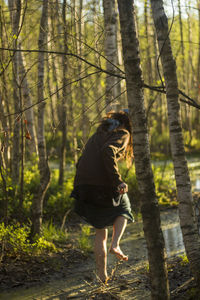 Woman running on field amidst trees in forest