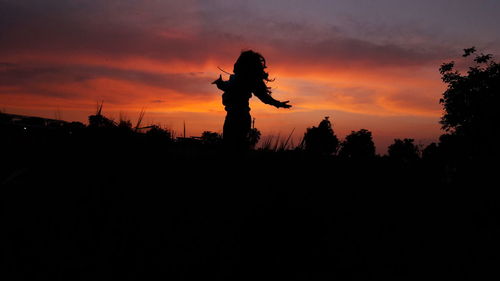 Silhouette woman standing by tree against orange sky