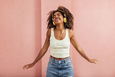 Young woman listening music while standing against wall