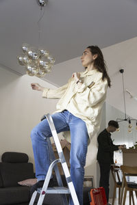 Young woman installing chandelier while relocating at home