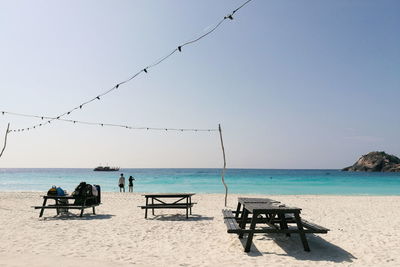 Picnic tables on sand at beach against sky